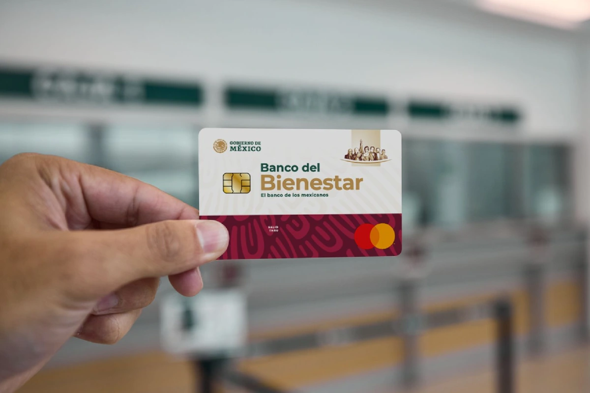 Tarjeta del banco del bienestar y en el fondo difuminado una sucursal del banco del bienestar