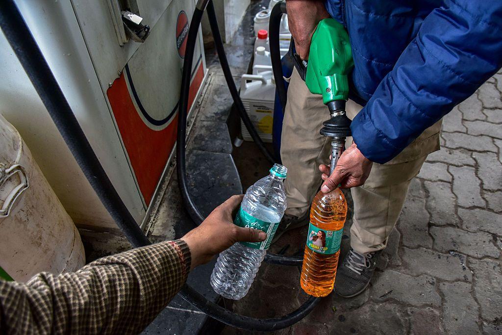 Unos hombres llenan unas botellas con gasolina en una estación de servicio.
